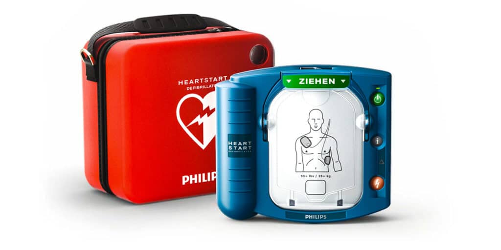 Rotes Philips Heartstart HS1 AED Trageetui neben einem blauen Defibrillator auf weißem Hintergrund