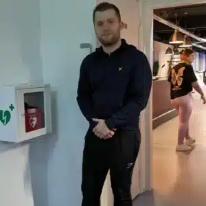 Mann mit dunklem Pullover steht neben AED-Wandschrank