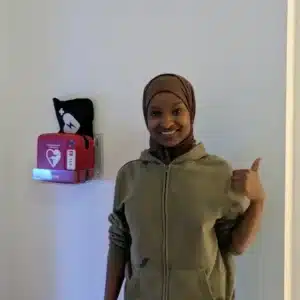 Junger Mann zeigt auf AED an weißer Wand