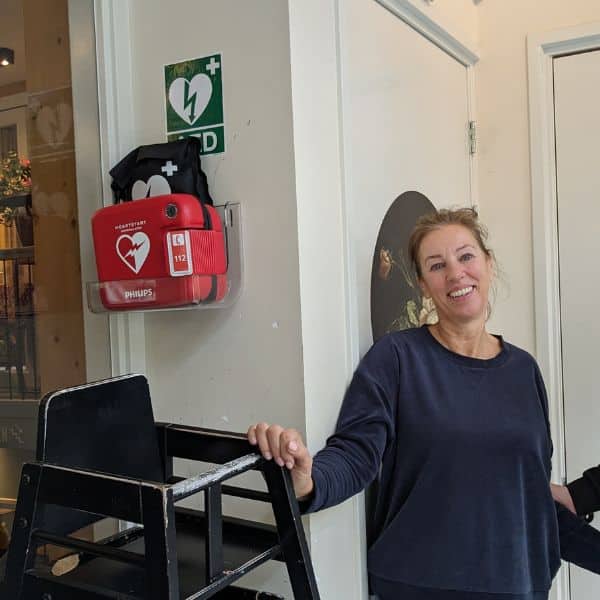 Frau präsentiert montierten AED an der Wand