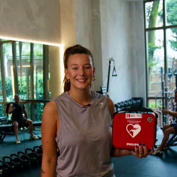 Frau hält roten Defibrillatorkoffer im Fitnessstudio